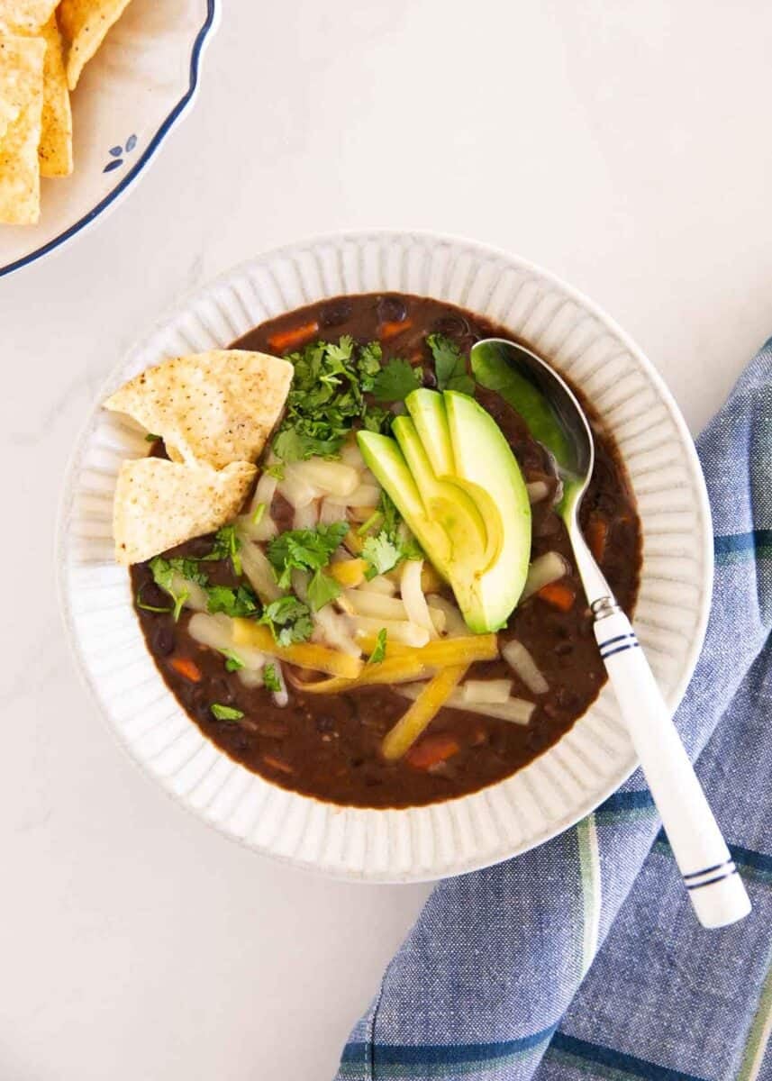 Bowl of black bean soup topped with avocado, cilantro, cheese and tortilla chips.