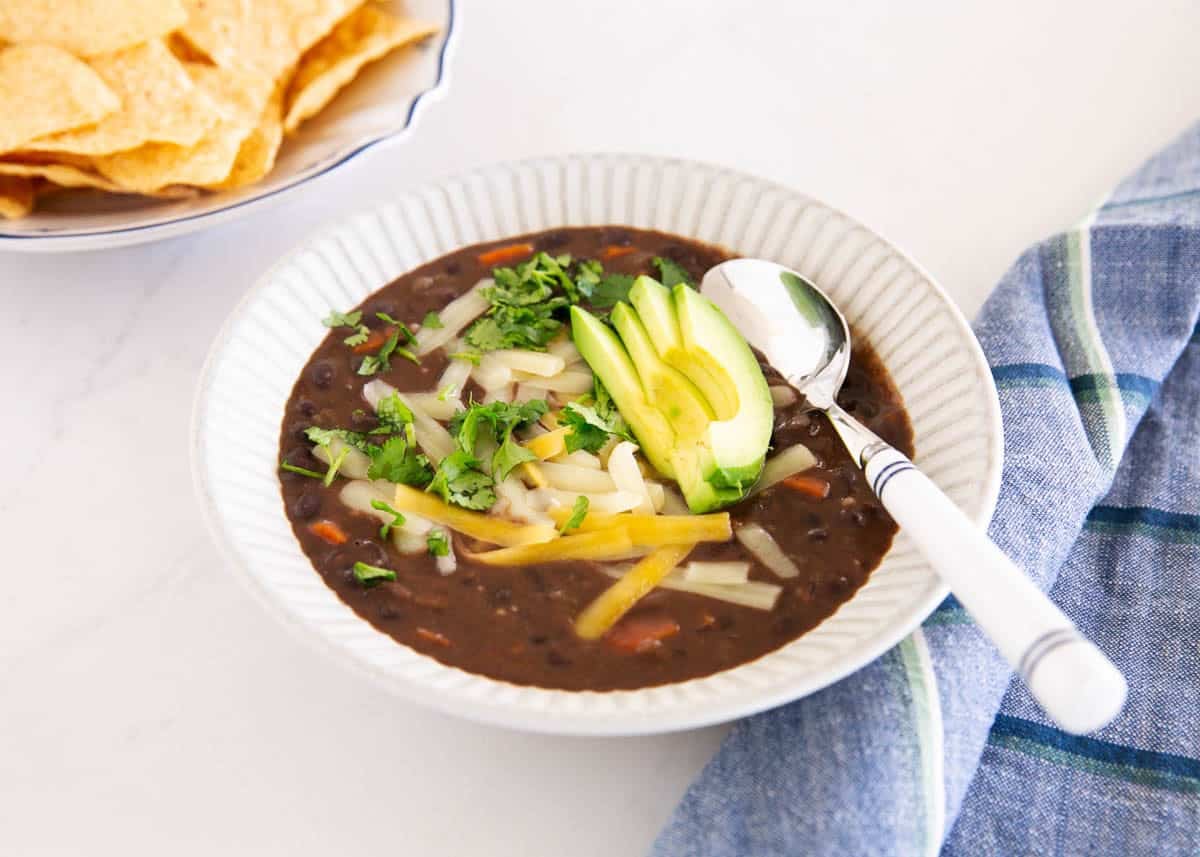 Homemade black bean soup with avocado, cilantro and cheese served with tortilla chips.