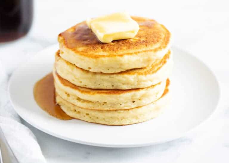 A stack of fluffy buttermilk pancakes on a plate with a pat of butter.