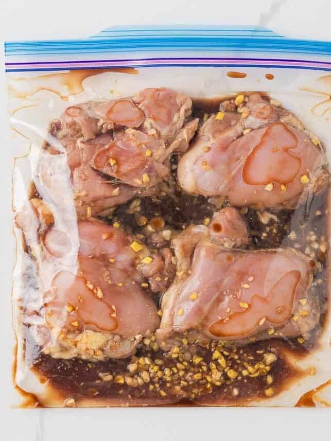 Chicken thighs marinating in a soy sauce, honey, garlic and ginger marinade inside a zip-top bag.