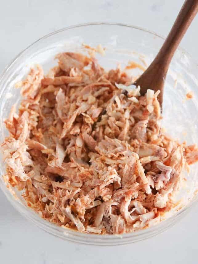 Shredded chicken mixed with cheese, salsa and seasoning in a glass bowl.