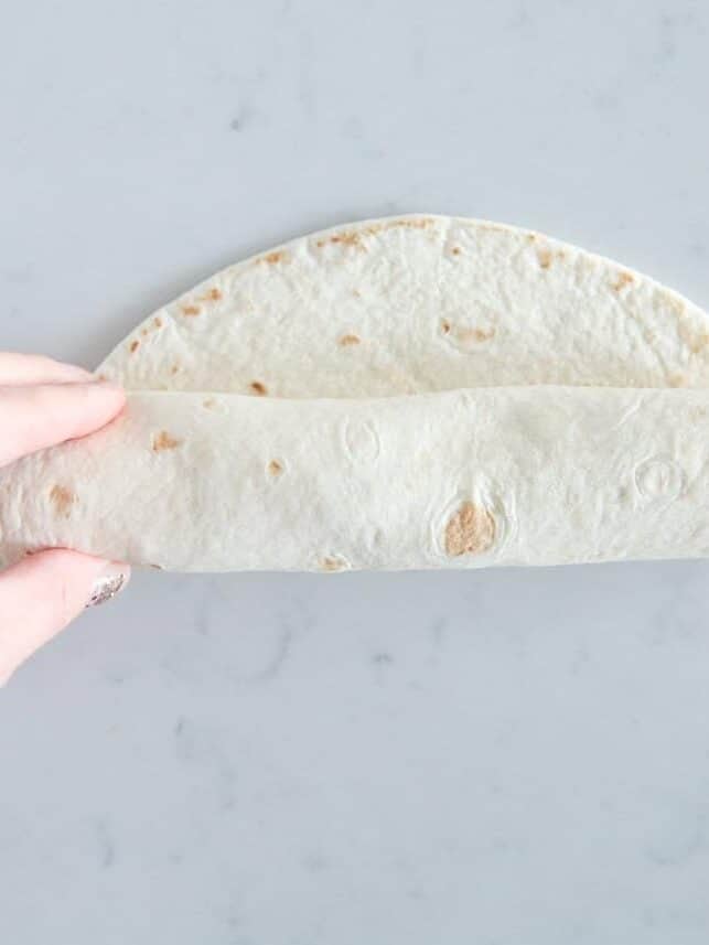 Rolling a flour tortilla tightly around the chicken filling.