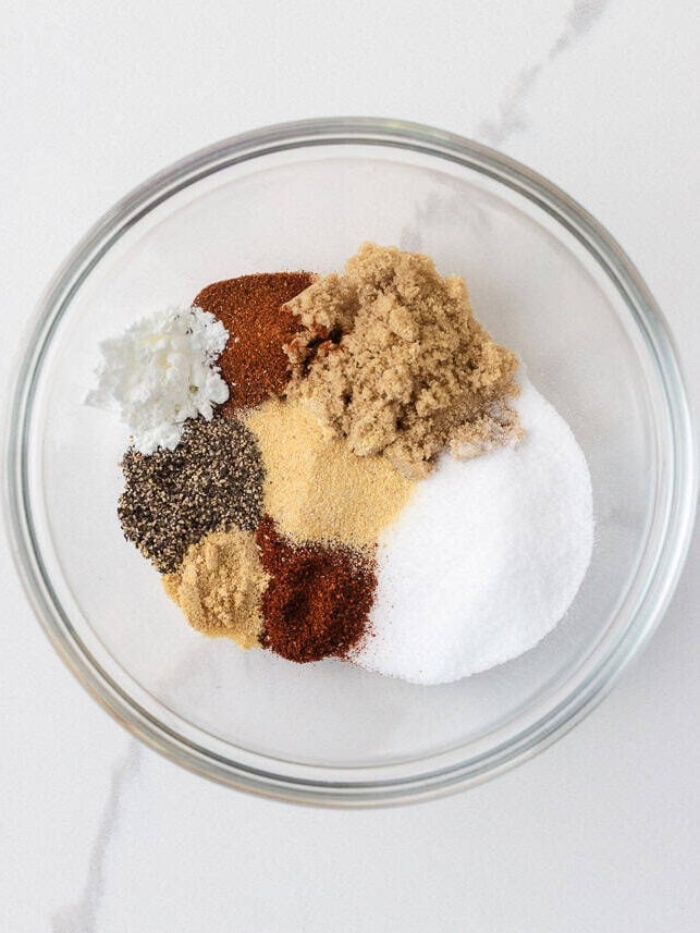 Dry steak rub ingredients in a glass bowl with salt, brown sugar, paprika, chili powder, garlic powder and pepper.