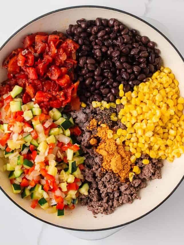 Cooked ground beef, zucchini, black beans, corn, fire roasted tomatoes and taco seasoning arranged in a skillet before stirring together.