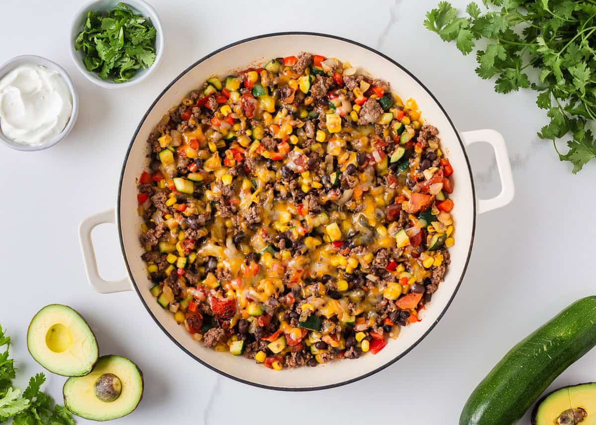 Cheesy zucchini beef skillet with ground beef, corn, black beans and tomatoes, ready to serve with avocado and cilantro.