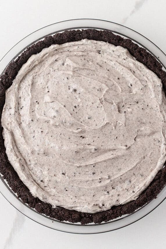 No bake Oreo cheesecake filling spread evenly into an Oreo cookie crust.