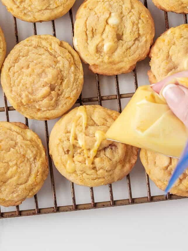 Drizzling orange glaze over baked orange creamsicle cookies on a cooling rack.