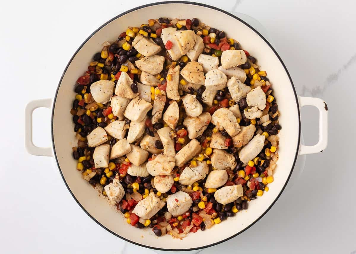 Cooked chicken mixed with black beans, fire-roasted corn, tomatoes and onions in a skillet.