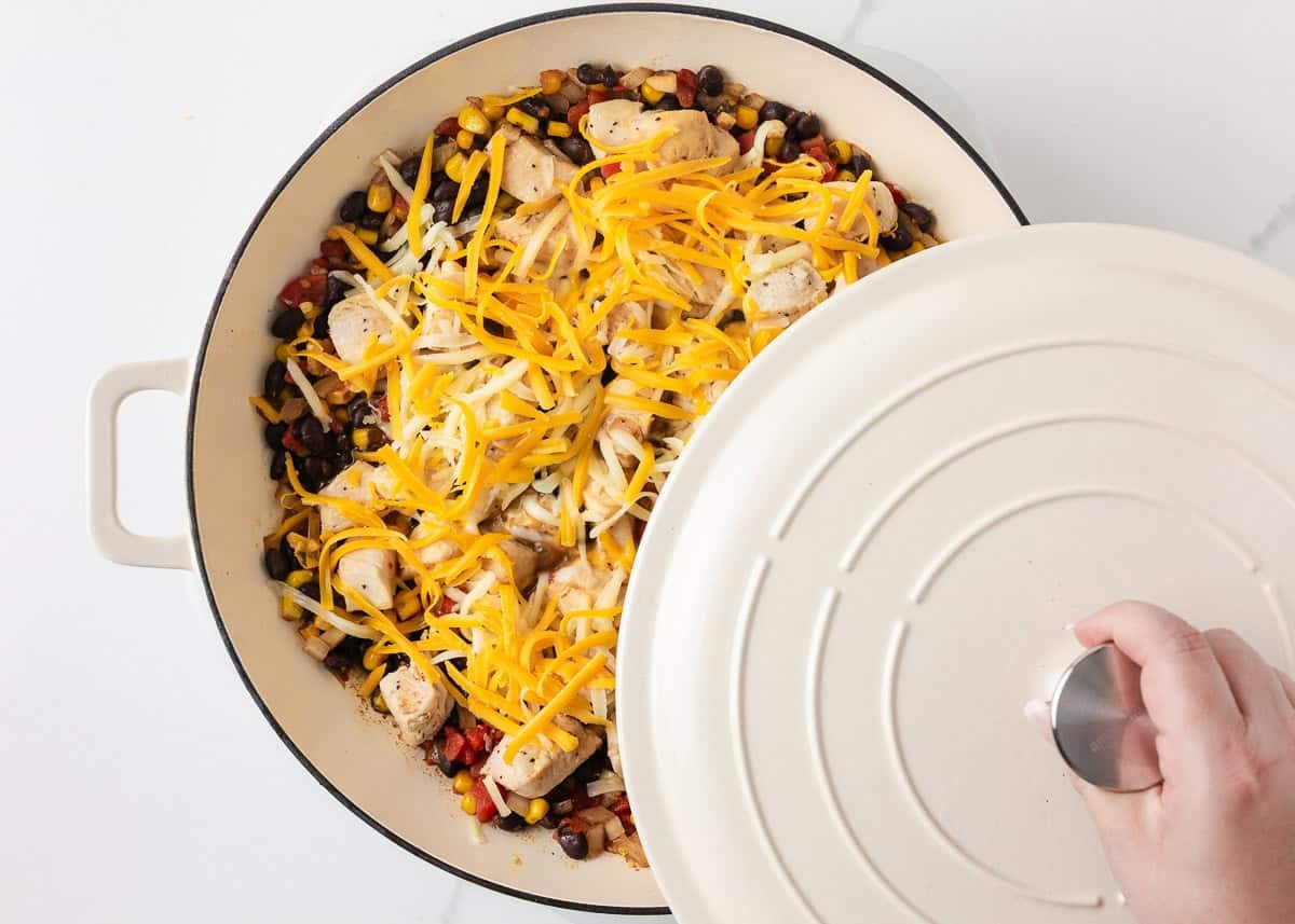 Shredded cheese being added to Santa Fe chicken with black beans, corn and tomatoes in a skillet.
