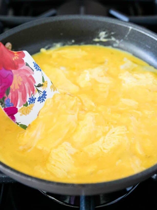Pulling scrambled eggs to the center of the pan with a spatula.