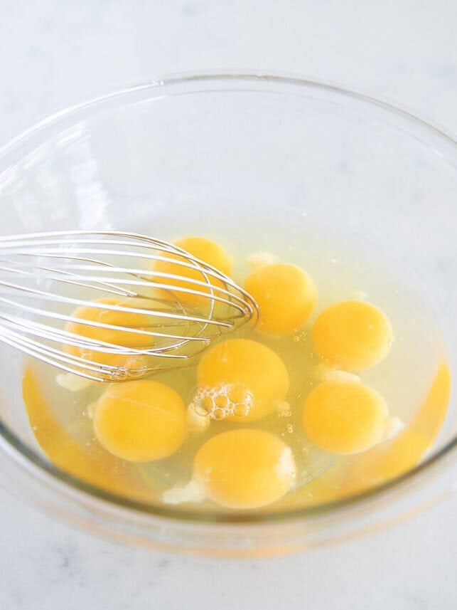 Whisking large eggs in a glass bowl.