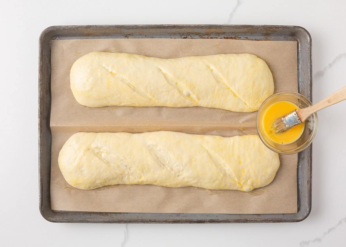 Shaped sourdough French bread loaves brushed with egg wash before baking.