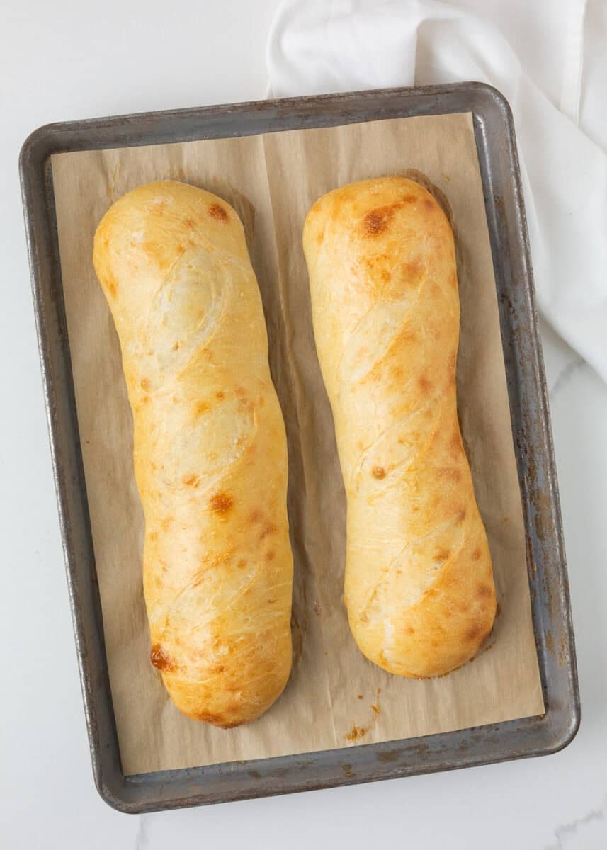 Two golden loaves of sourdough French bread cooling on a parchment-lined baking sheet.