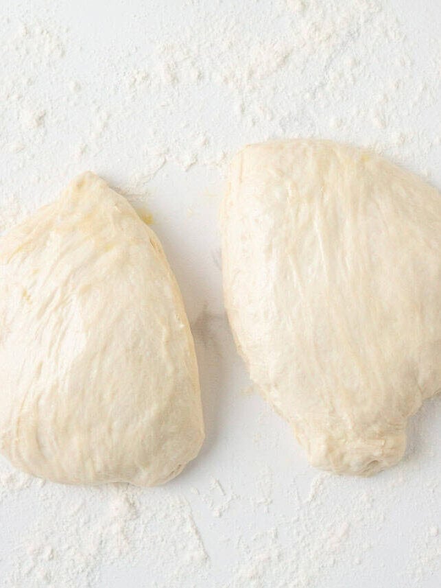 Two pieces of sourdough French bread dough divided on a lightly floured surface.