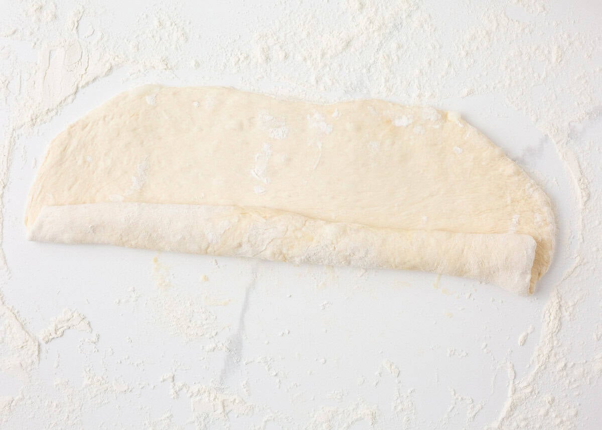 Sourdough French bread dough rolled into a rectangle and starting to form a loaf.