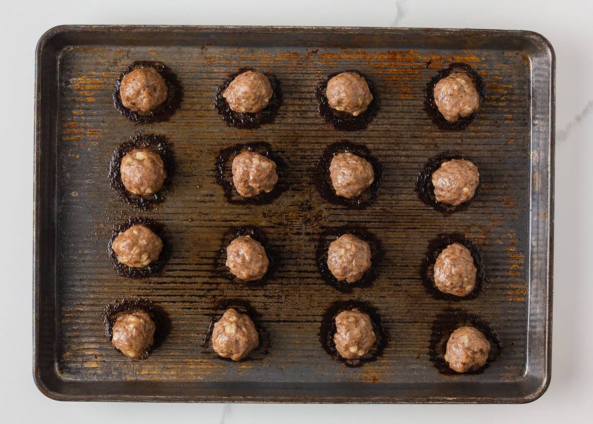 Baked pork meatballs on a sheet pan before being tossed in sticky Asian sauce.