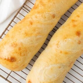 Fresh sourdough French bread loaves cooling on a wire rack with a golden crust.