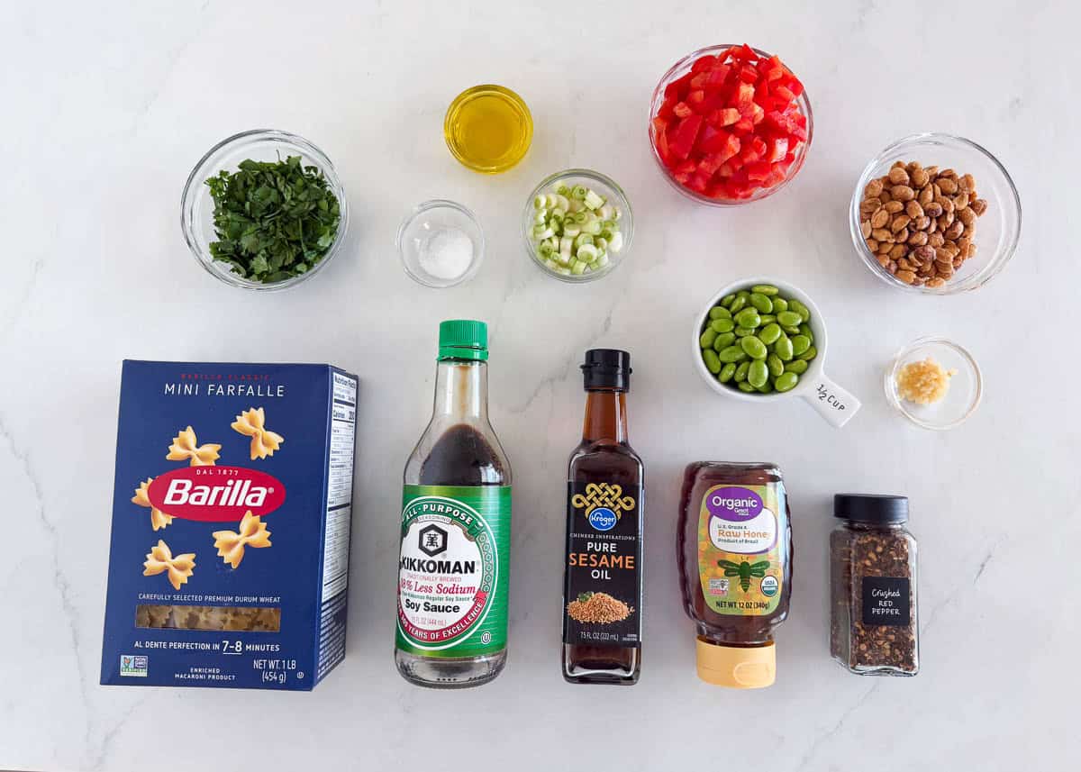 Ingredients for Thai pasta salad including mini farfalle, soy sauce, sesame oil, honey, crushed red pepper, edamame, red bell pepper, peanuts, cilantro, green onions, and garlic.