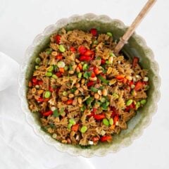 Overhead view of Thai pasta salad with peanut dressing in a green scalloped bowl with a wooden spoon.