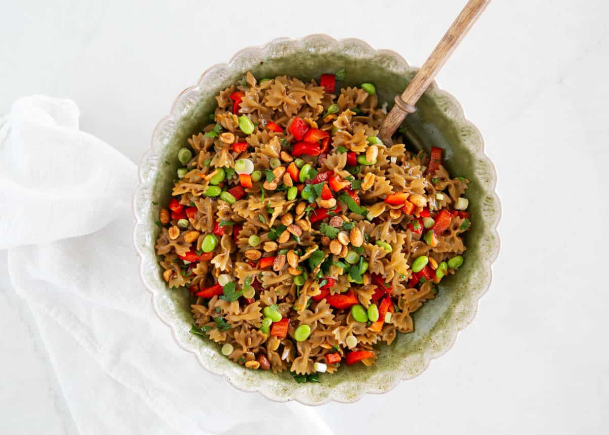 Overhead view of Thai pasta salad with peanut dressing in a green scalloped bowl with a wooden spoon.