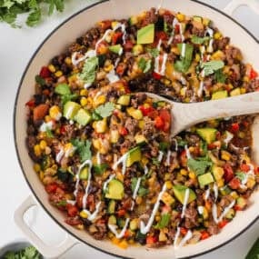 Zucchini beef skillet topped with melted cheese, avocado, cilantro and sour cream in a large cream-colored pan.