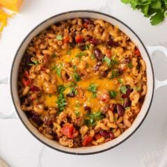 Overhead view of homemade chili mac with ground beef, kidney beans, elbow pasta, tomatoes and melted cheddar cheese in a white Dutch oven.