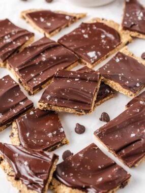 Viral cookie dough bark broken into pieces with chocolate chips and flaky sea salt on counter.