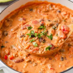 Creamy taco soup with ground beef, beans, corn and tomatoes being lifted from a white Dutch oven with a wooden ladle.