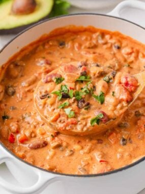 Creamy taco soup with ground beef, beans, corn and tomatoes being lifted from a white Dutch oven with a wooden ladle.