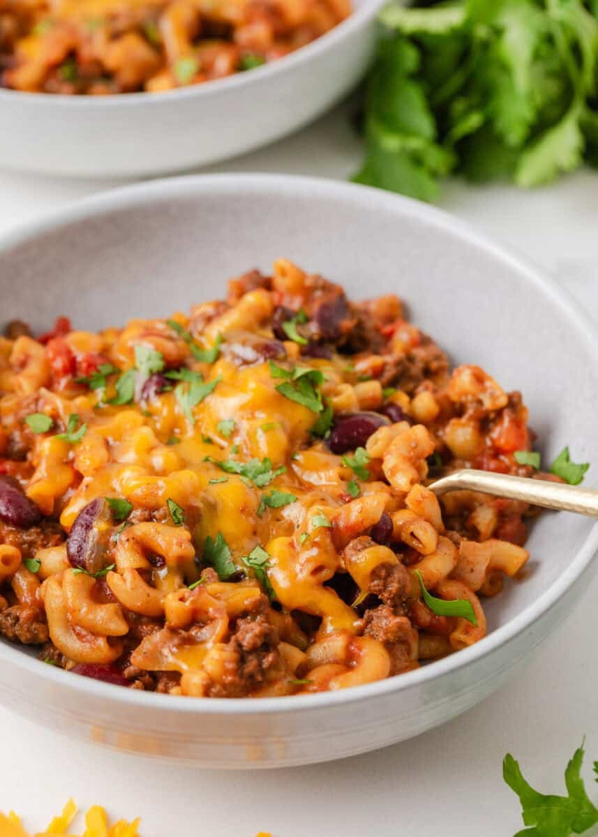 Close-up bowl of cheesy chili mac with ground beef, kidney beans and elbow pasta, topped with chopped cilantro.