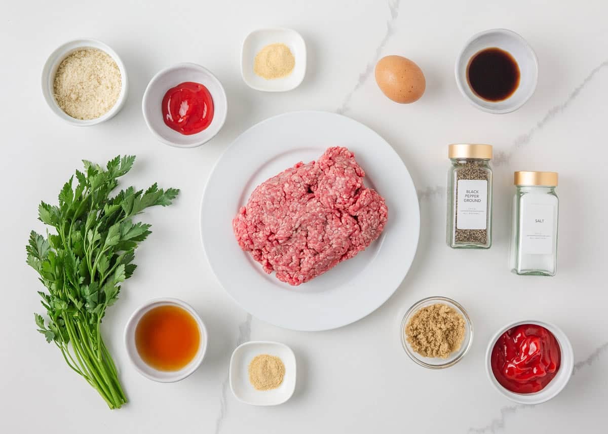 Ingredients for a mini meatloaf recipe including ground beef, breadcrumbs, egg, ketchup, parsley and seasonings.