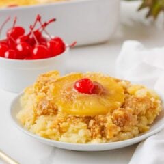 Close-up of pineapple dump cake on a plate topped with a pineapple ring and maraschino cherry.