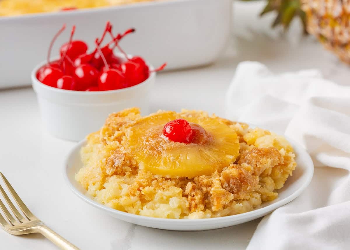 Close-up of pineapple dump cake on a plate topped with a pineapple ring and maraschino cherry.