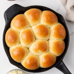Overhead view of soft, golden dinner rolls baked in a cast iron skillet with butter and jam.