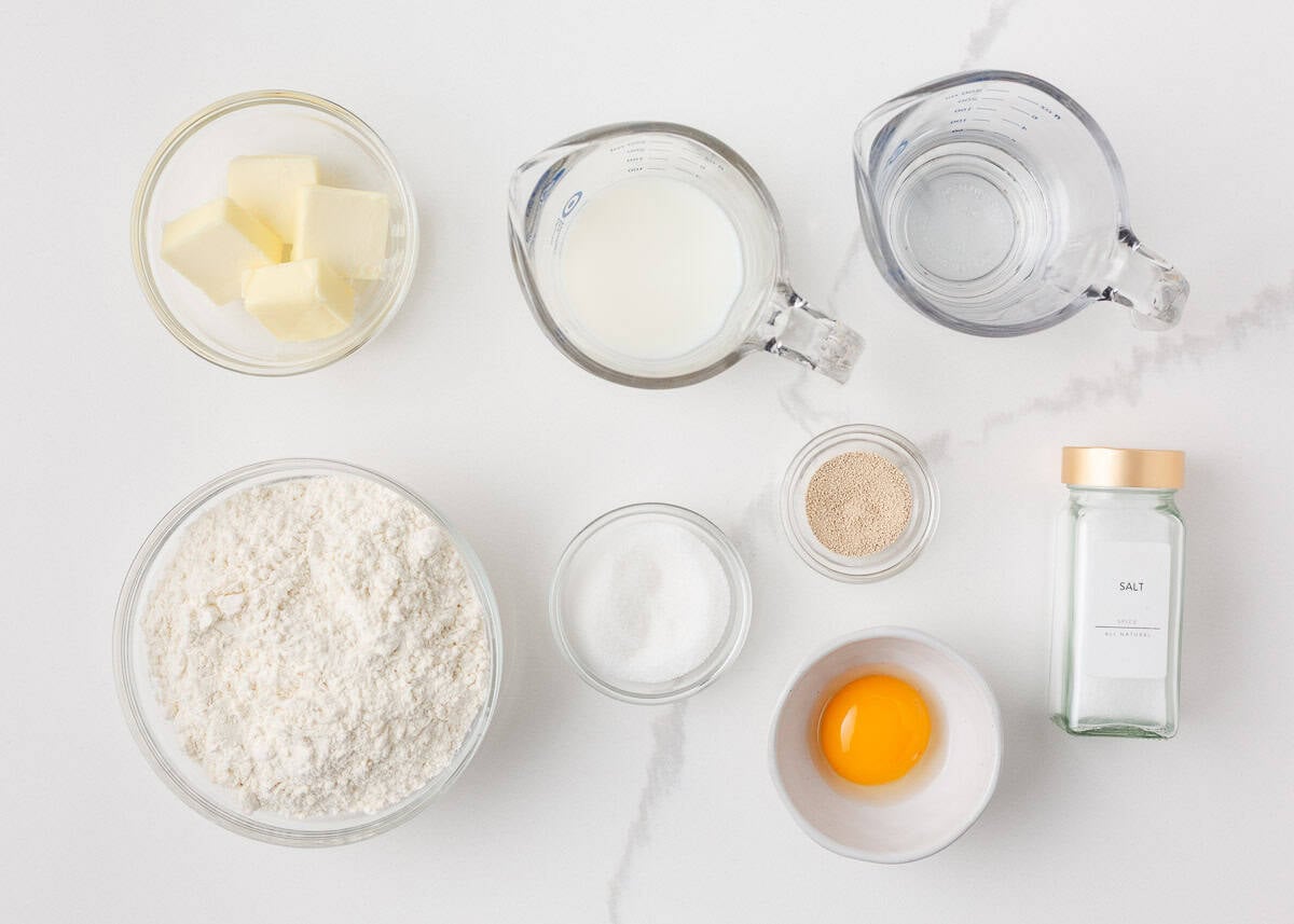 Ingredients for homemade skillet rolls, including flour, yeast, sugar, butter, milk, water, salt and egg yolk.