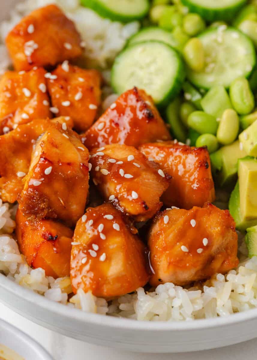 Close-up of tender teriyaki salmon bites glazed with sauce and sprinkled with sesame seeds over rice.