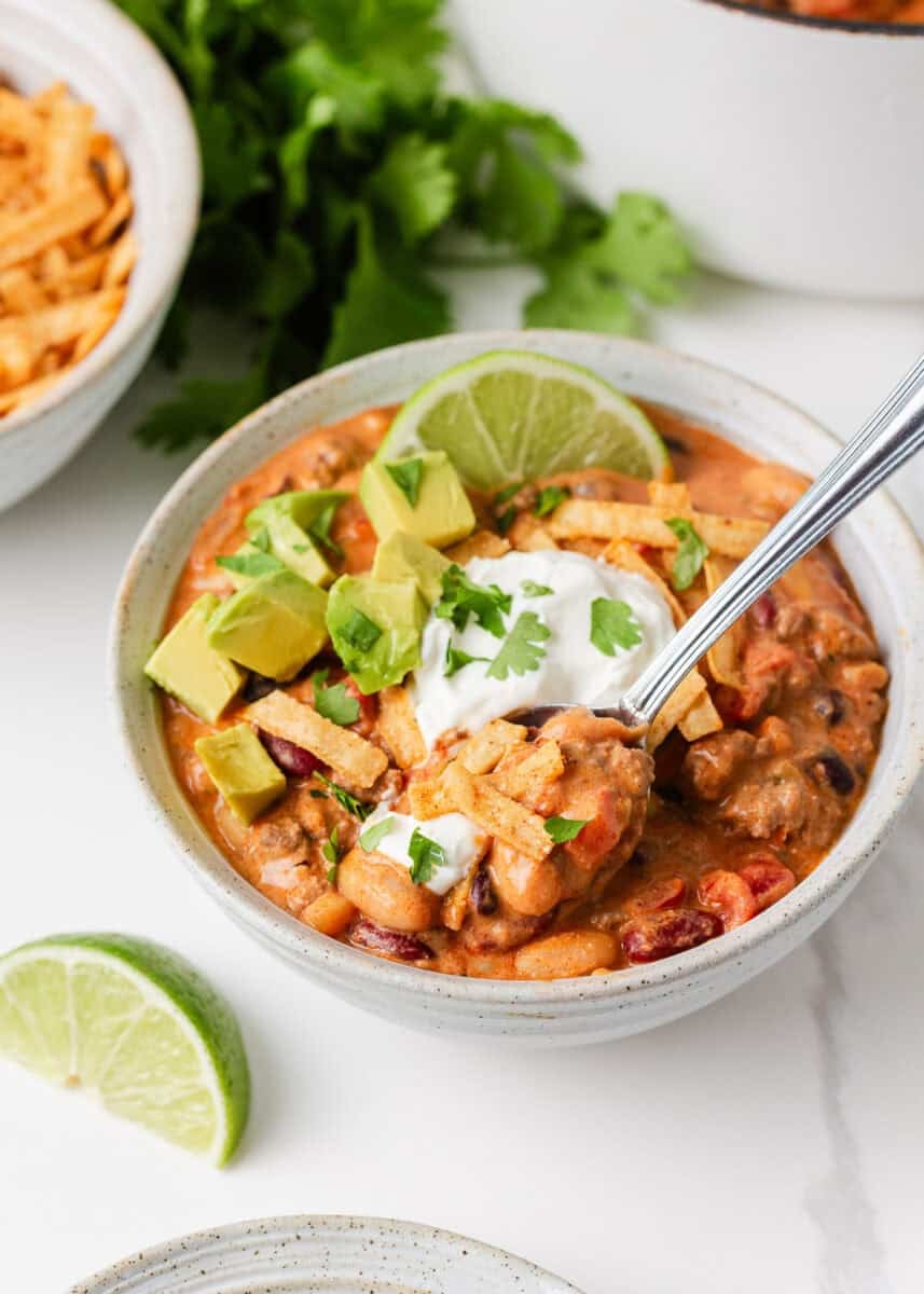 Bowl of creamy taco soup topped with avocado, sour cream, cilantro and tortilla strips, served with fresh lime.