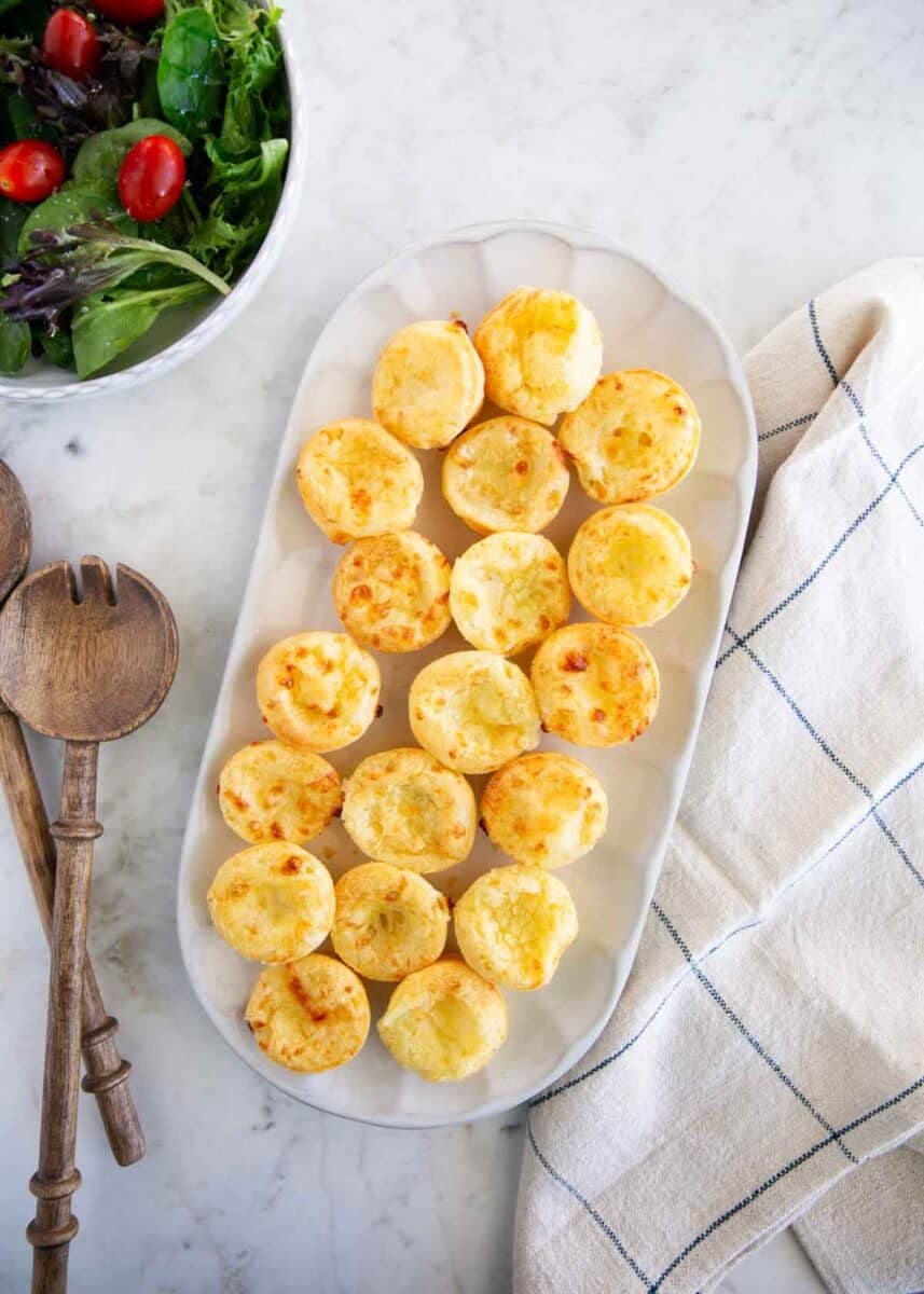 Brazilian cheese bites served on a platter with a fresh green salad.