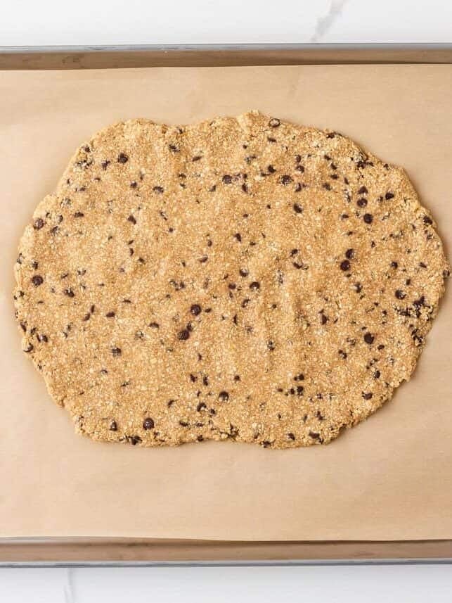 Oat cookie dough mixture pressed onto a parchment-lined baking sheet for homemade cookie dough bark.