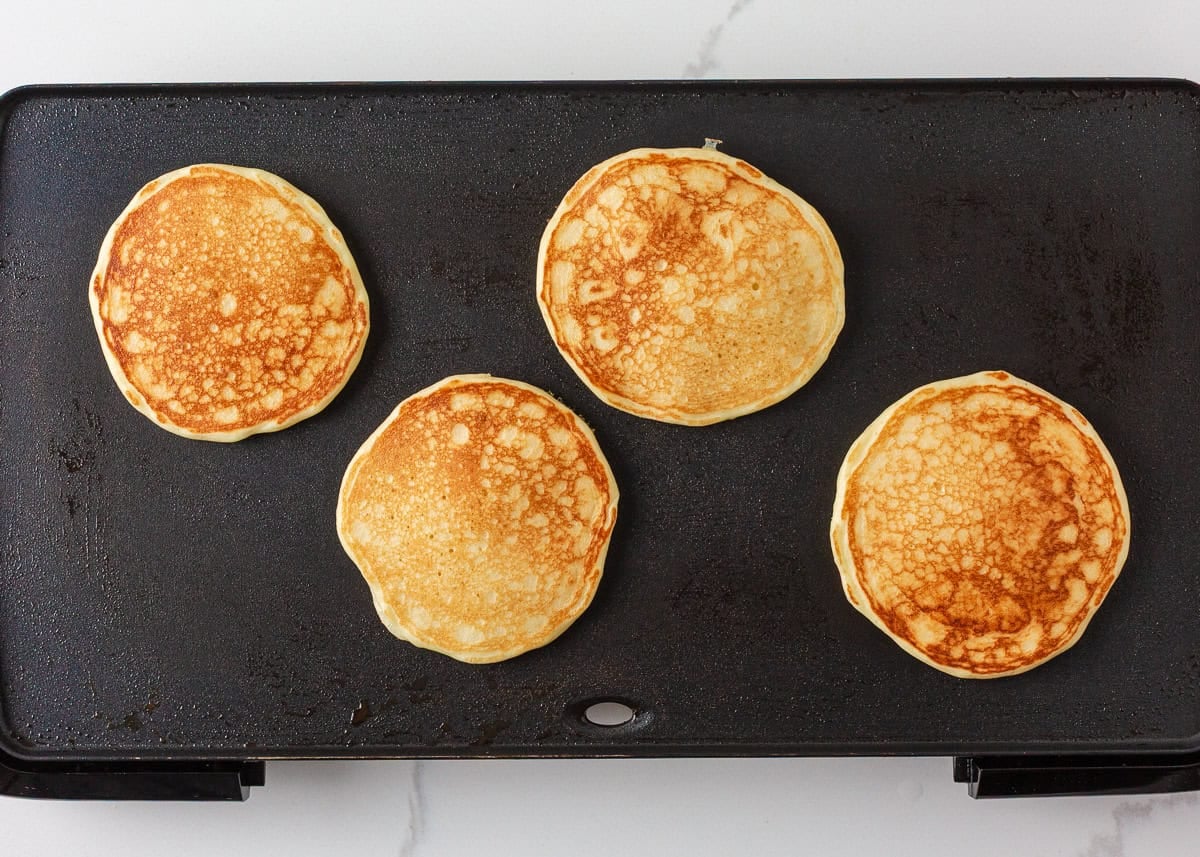 Four cottage cheese pancakes flipped and cooked until golden brown on a griddle.