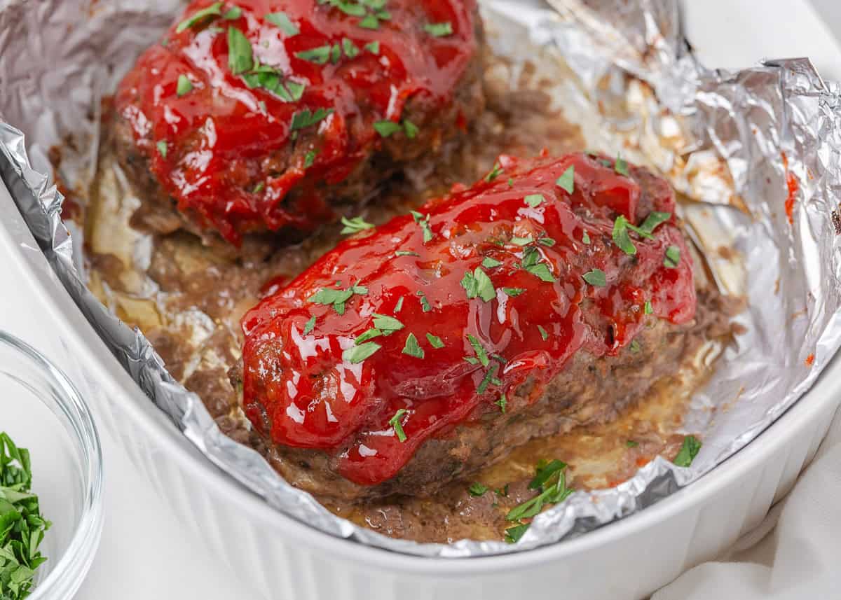 Baked mini meatloaves topped with ketchup glaze and parsley in a foil-lined baking dish.