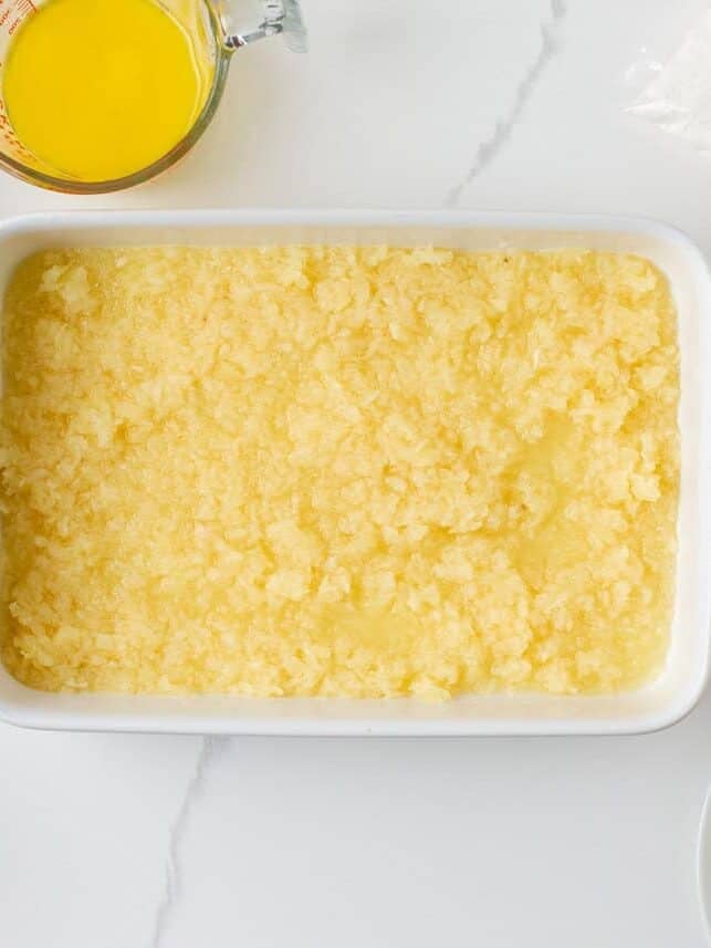 Crushed pineapple spread evenly in the bottom of a white baking dish for pineapple dump cake.