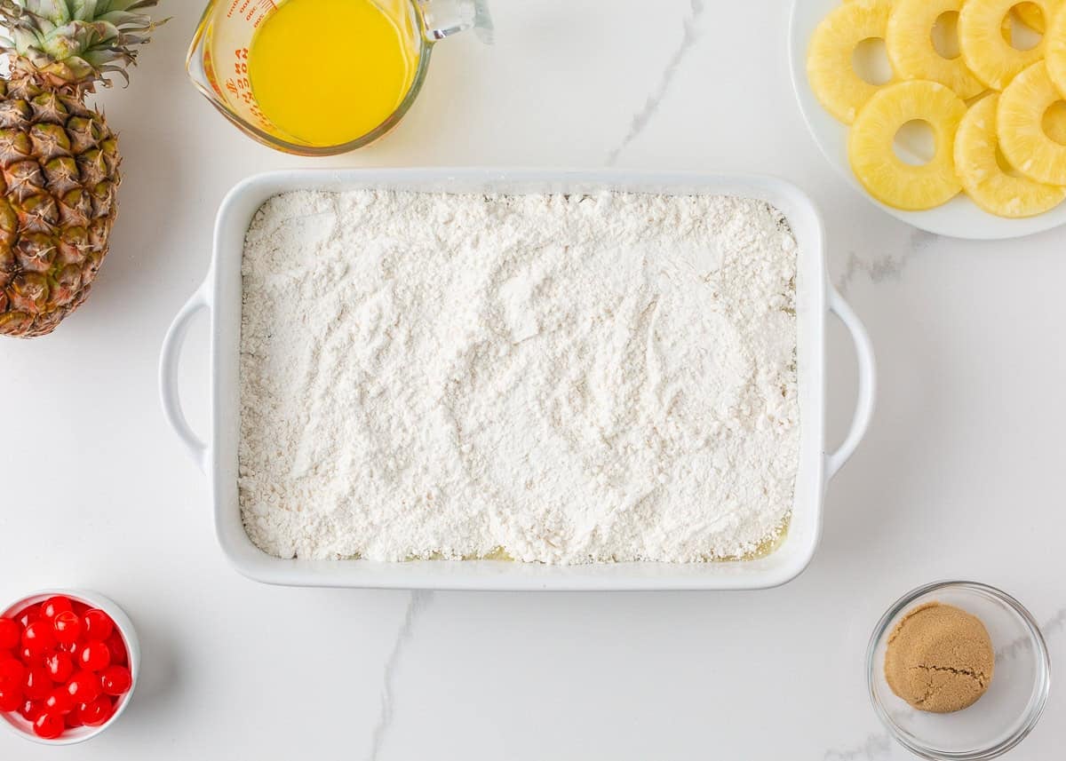 Dry yellow cake mix sprinkled over crushed pineapple in a white baking dish.