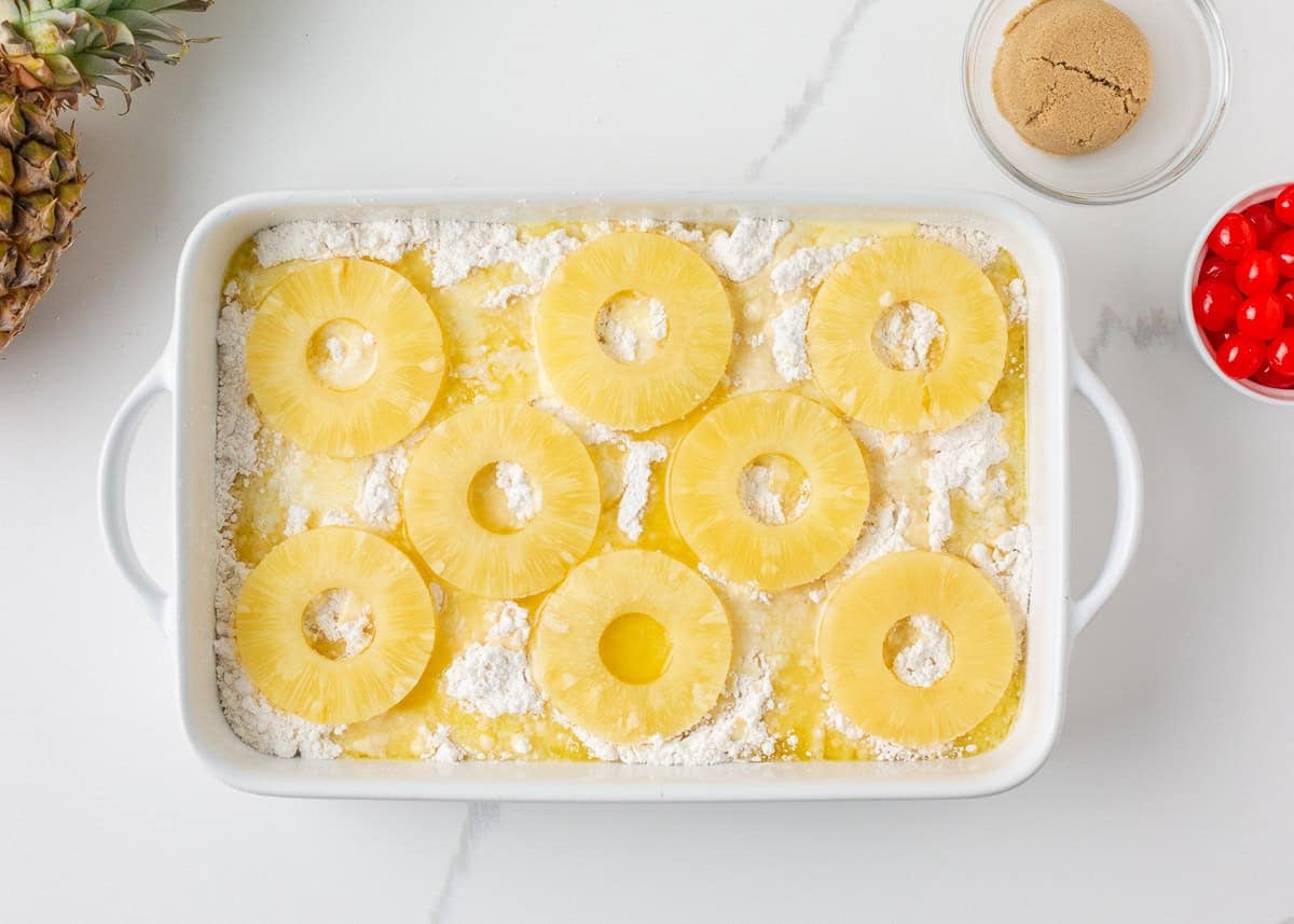 Pineapple rings arranged over cake mix and butter in a white casserole dish.