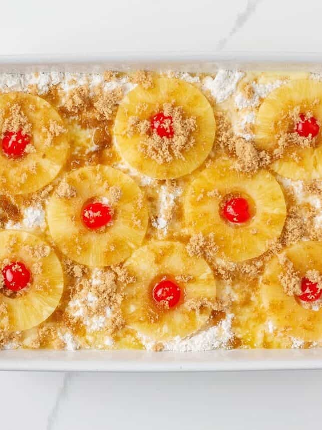 Pineapple rings, cherries, and brown sugar layered on top of pineapple dump cake before baking.