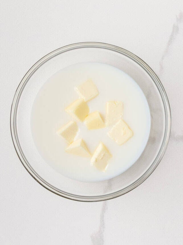 Cubed butter and milk in a glass bowl for making homemade dinner rolls.