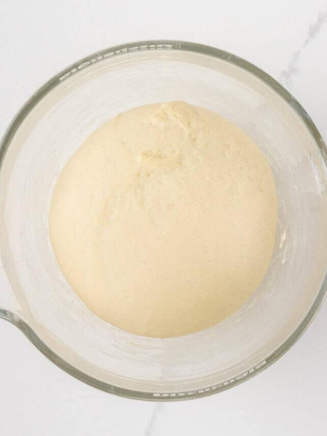 Soft dinner roll dough doubled in size in a glass stand mixer bowl.