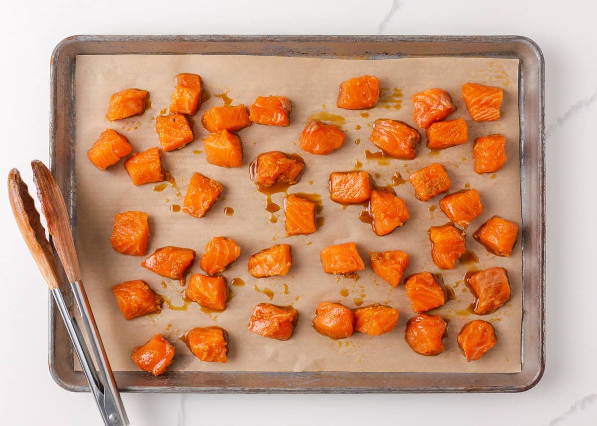 Broiled teriyaki salmon bites on a parchment-lined baking sheet.