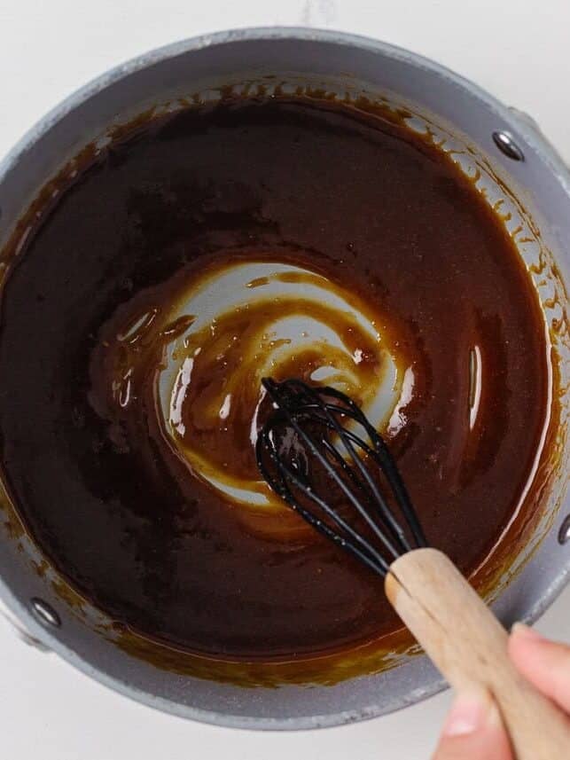 Thickened teriyaki glaze being whisked in a saucepan on the stovetop.
