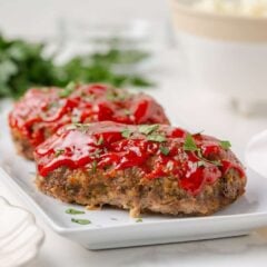 Two mini meatloaves topped with ketchup glaze and fresh parsley on a white serving platter.